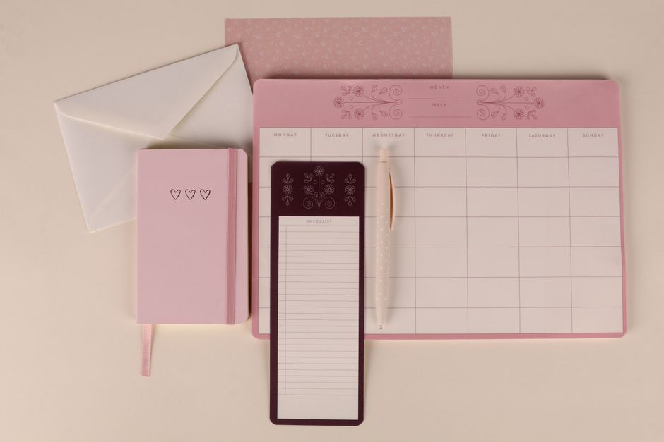 Elegant pink stationery flat lay with a planner, notebook, and checklist pad, perfect for organizing.